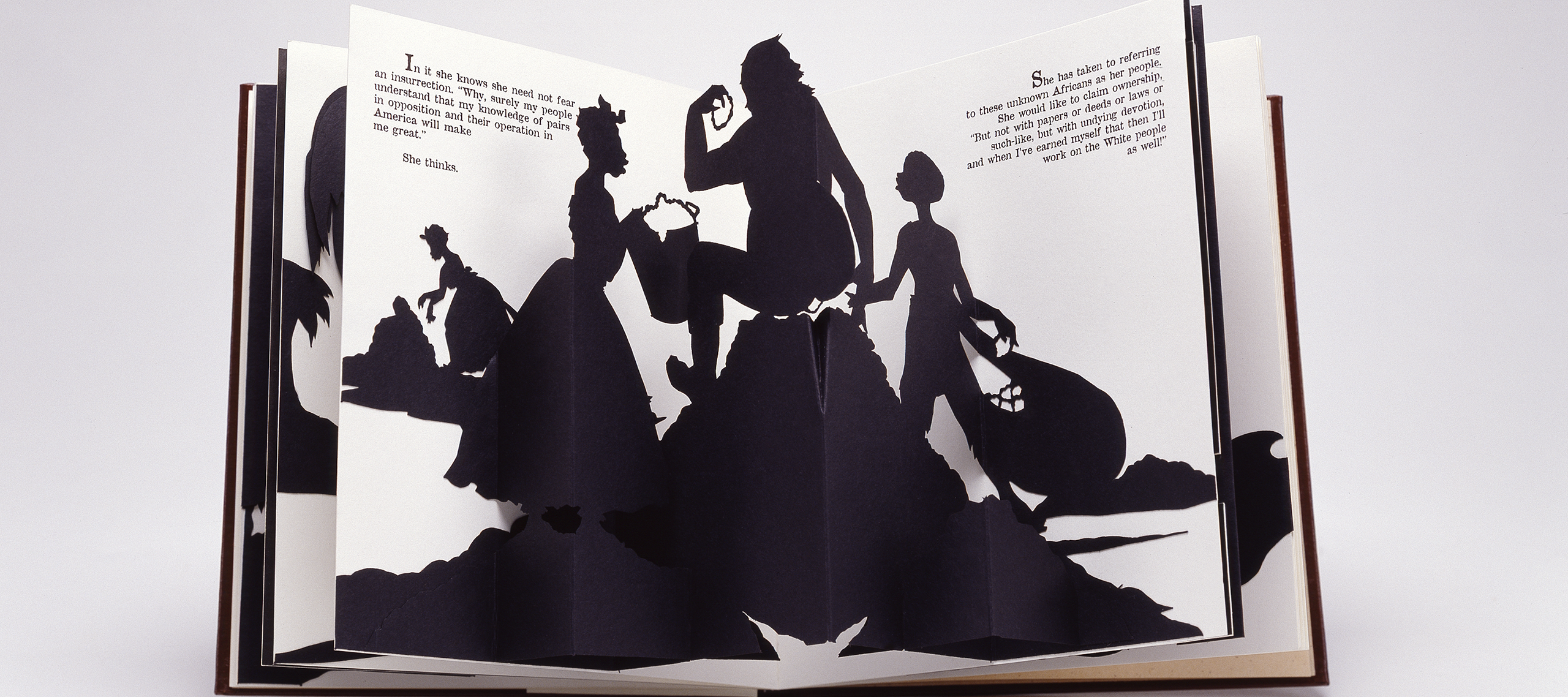 Four black silhouetted figures emerge from the white, open pages of a pop-up book. They appear to be engaged in manual labor. Two of the figures wear full floor-length skirts.