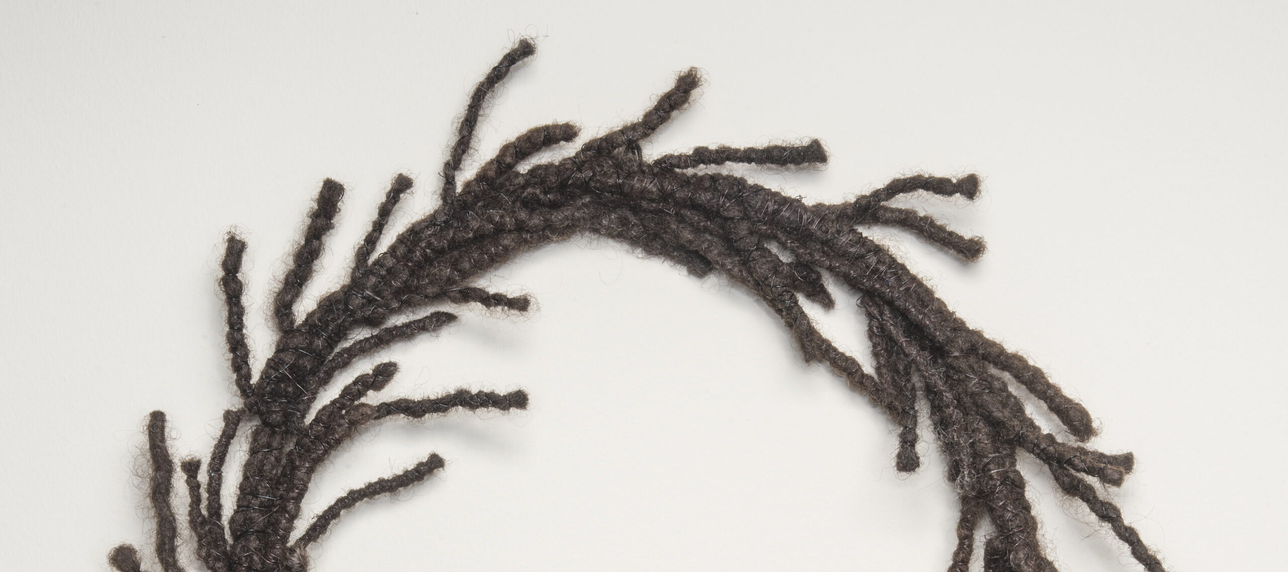 A circular wreath made of dark, tightly coiled hair with strands escaping and resembling laurels.