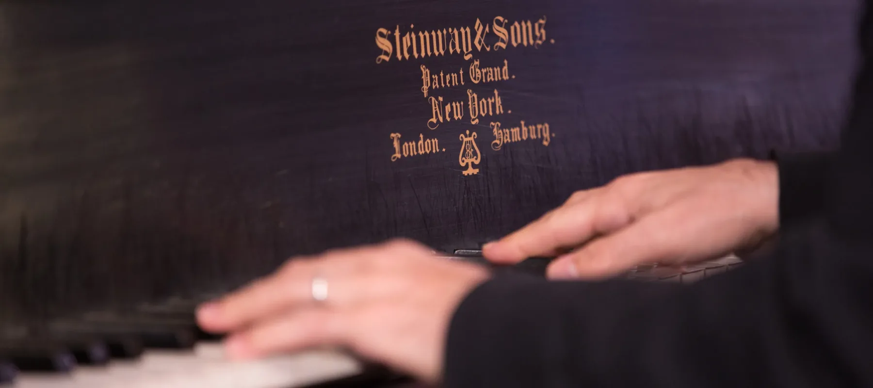 Two light-skinned hands in the middle of playing a black-and-white piano keyboard.