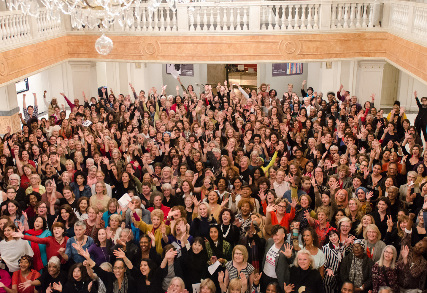 A color photograph of 435 women from a high vantage point. The women all look up towards the camera, some with arms outstretched.