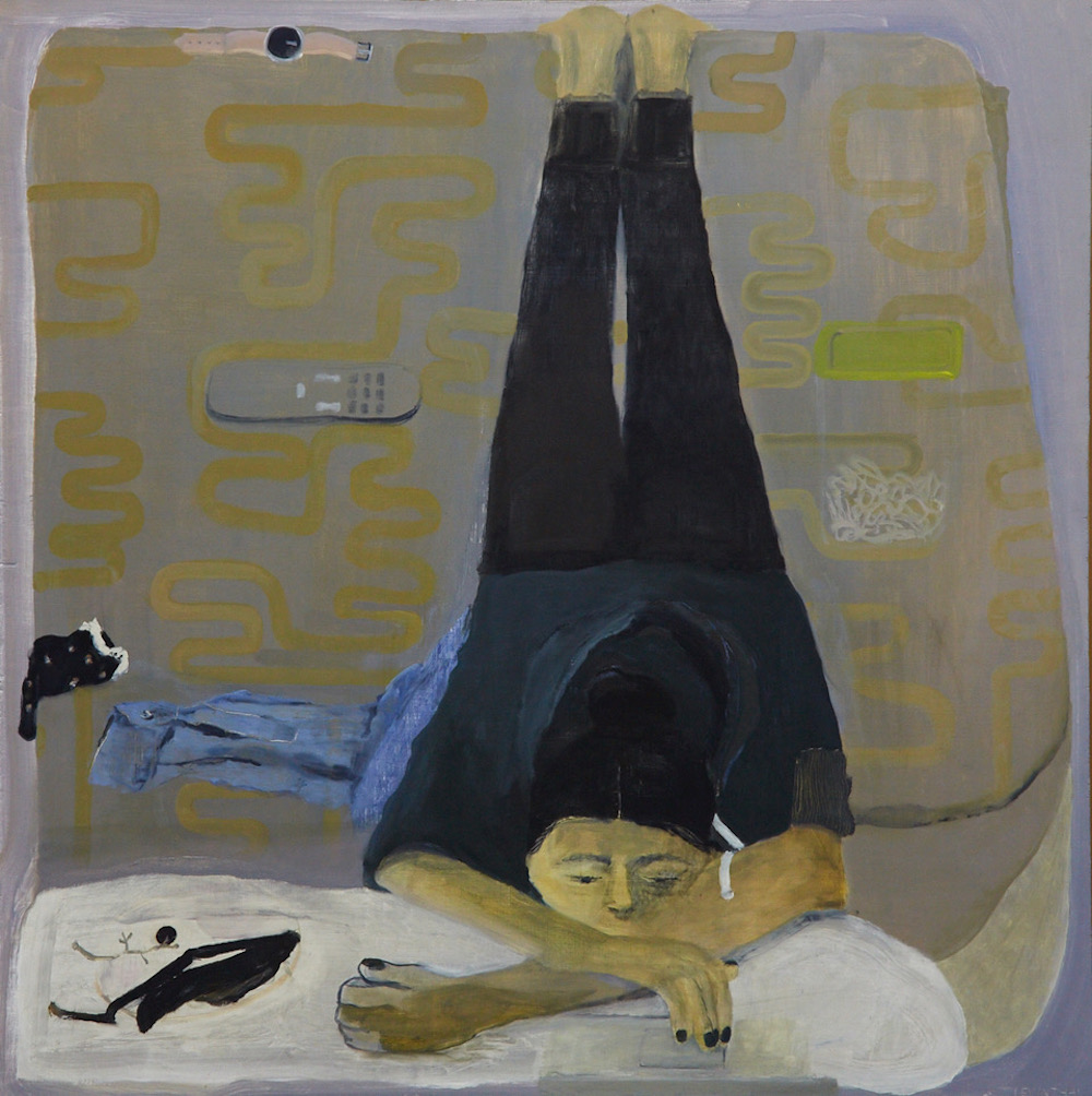 On a grey and yellow bedspread lies a sulking woman with medium skin, her body contorted with her shoulders tense, arms crossed, and legs hyperextended. With her chin on a white body pillow, she stares forward into nothingness while wearing all black.