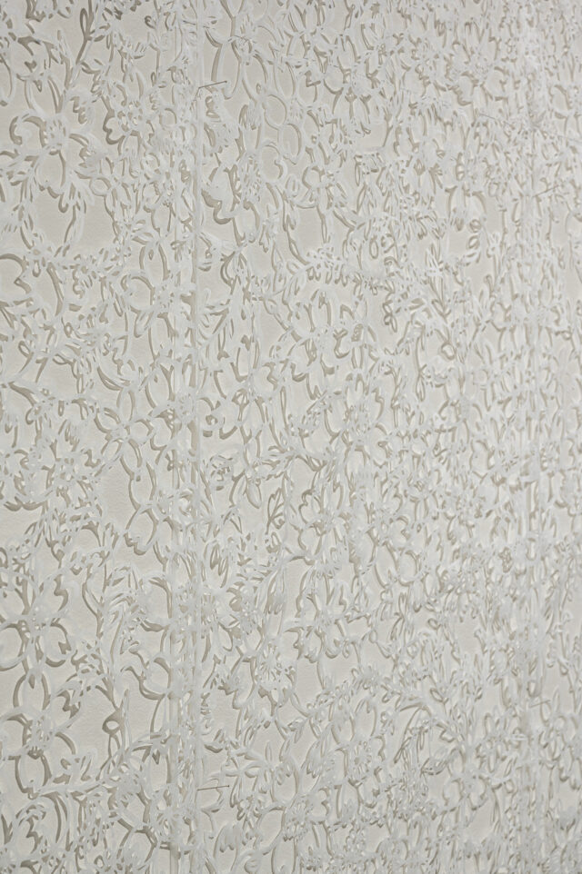 Delicately cut white tissue paper with floral patterns against a white wall. The cut paper casts shadows against the wall