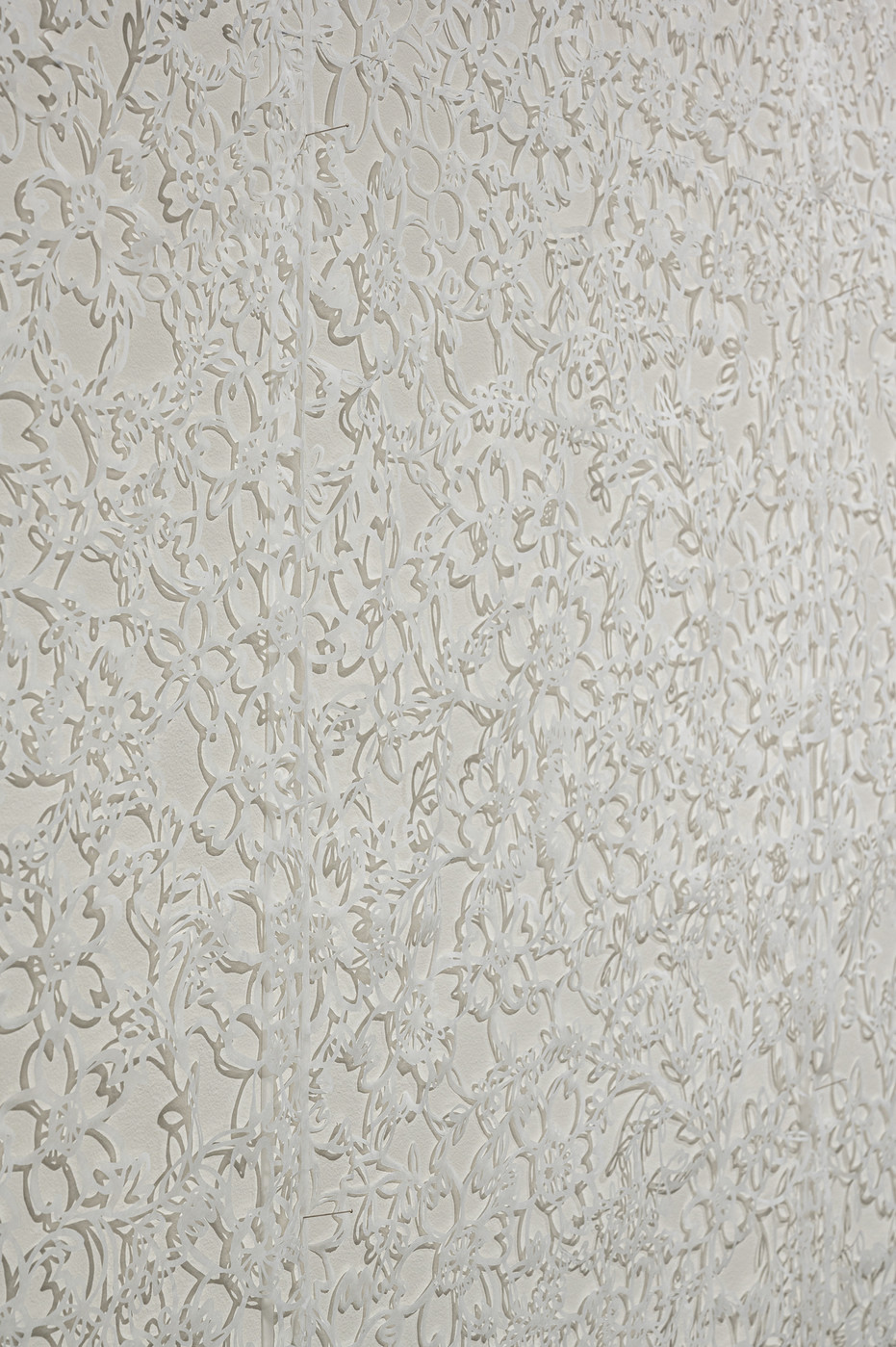 Delicately cut white tissue paper with floral patterns against a white wall. The cut paper casts shadows against the wall