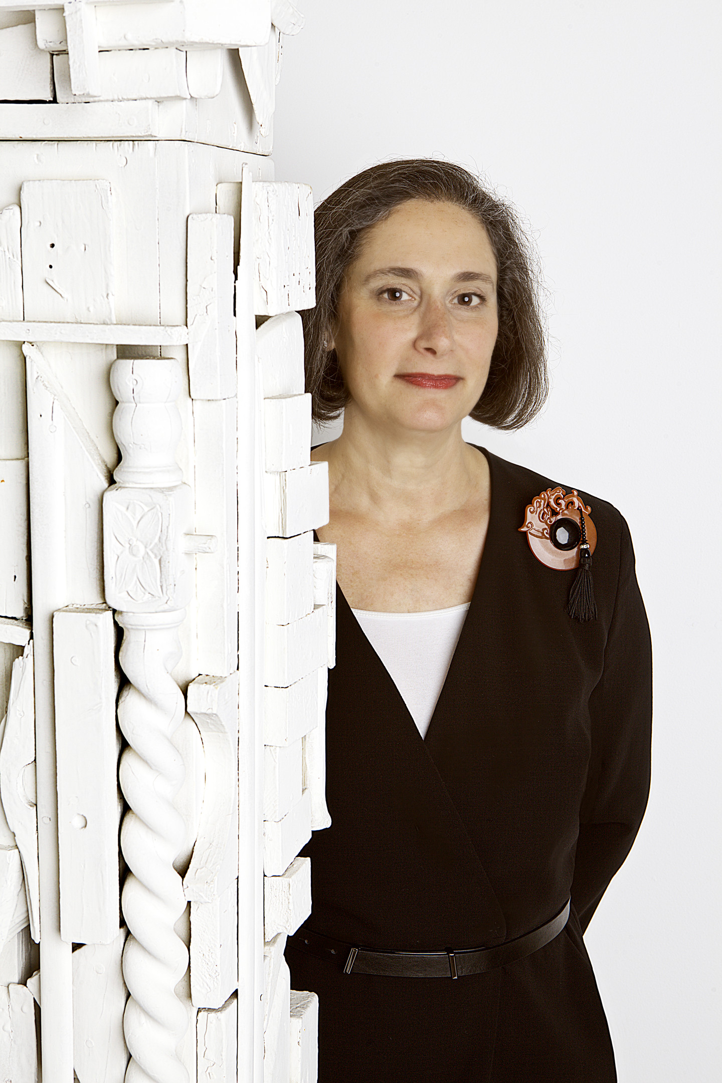 A woman with light skin and short brown hair posing behind a white assemblage sculpture.