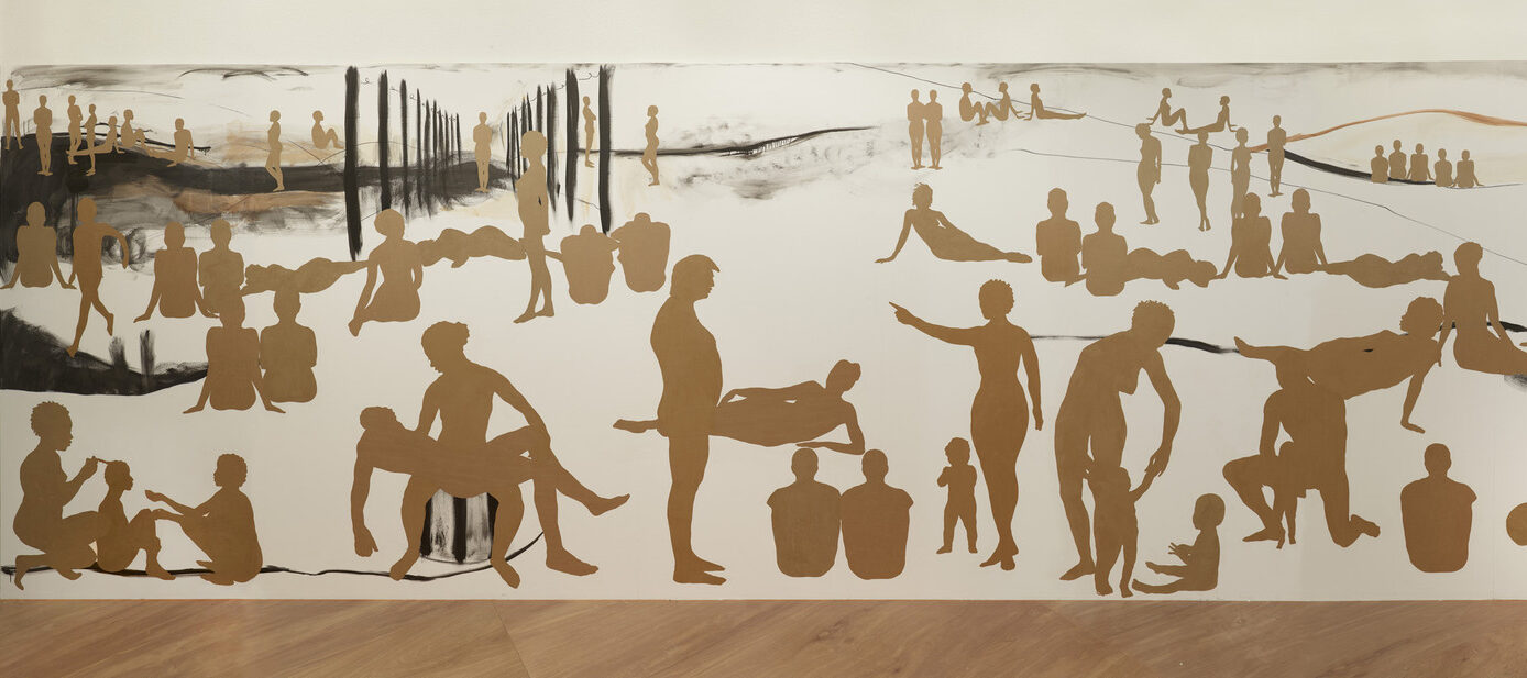 A long rectangular wall with many silhouetted figures made out of brown paper. The figures are of men, women and children in different positions as if in a landscape. They are different sizes to indicate foreground, middle ground and background.