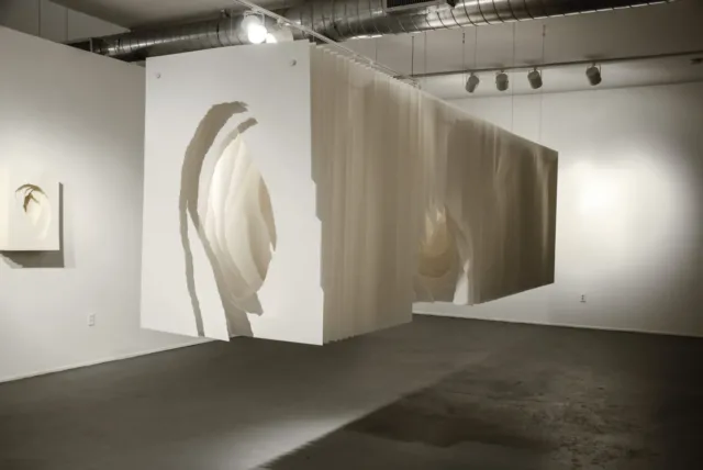 Panels of white paper hung together to look like a long rectangular box suspended from the ceiling a few feet off the ground. Roughly torn holes in the middle of the sheets create a tunnel-like space.