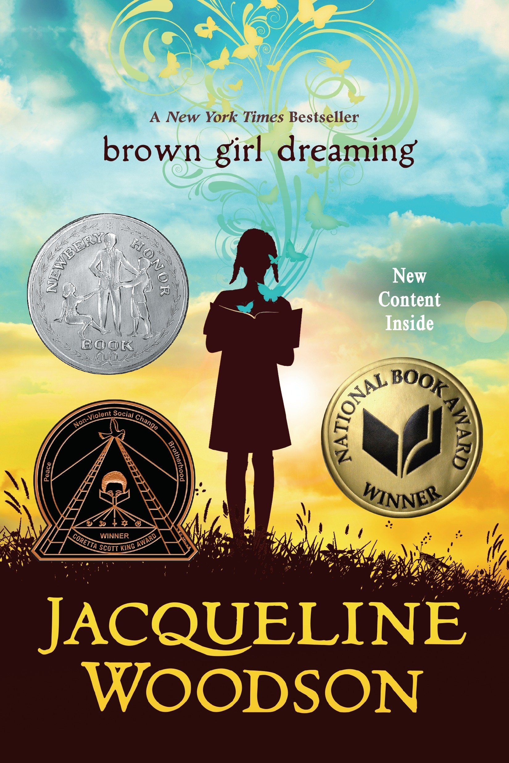 A book cover featuring the title "brown girls dreaming" in brown letters over a blue and white clouded sky. The silhouette of a young girl reading a book is positioned in the middle of the cover, in front of a golden sky. Three medals of honor surround her.