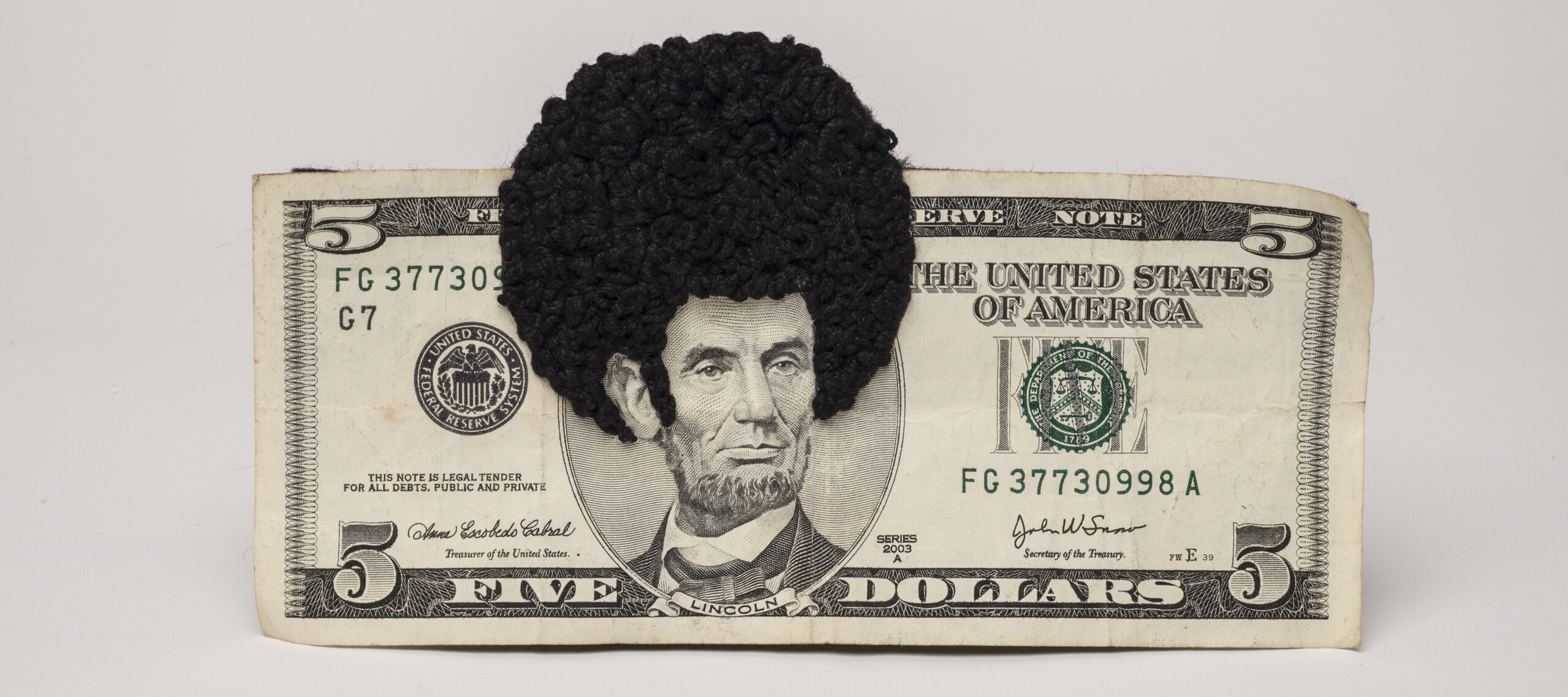 U.S. five-dollar bill has an embroidered afro and sideburns stitched onto the portrait of Lincoln’s head. One-third of the afro protrudes beyond the top of the bill.