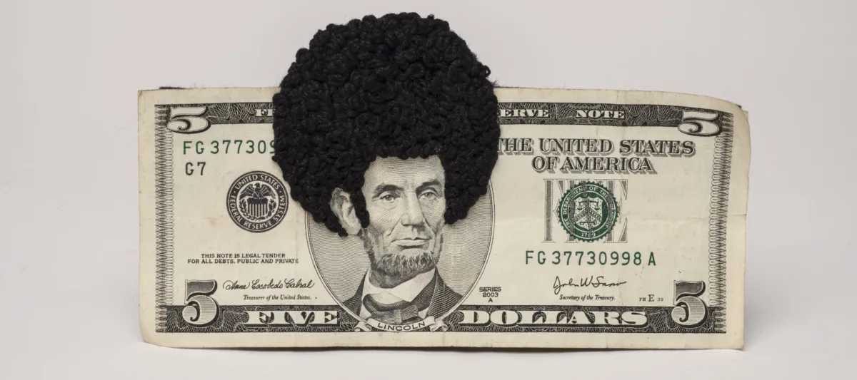 U.S. five-dollar bill has an embroidered afro and sideburns stitched onto the portrait of Lincoln’s head. One-third of the afro protrudes beyond the top of the bill.