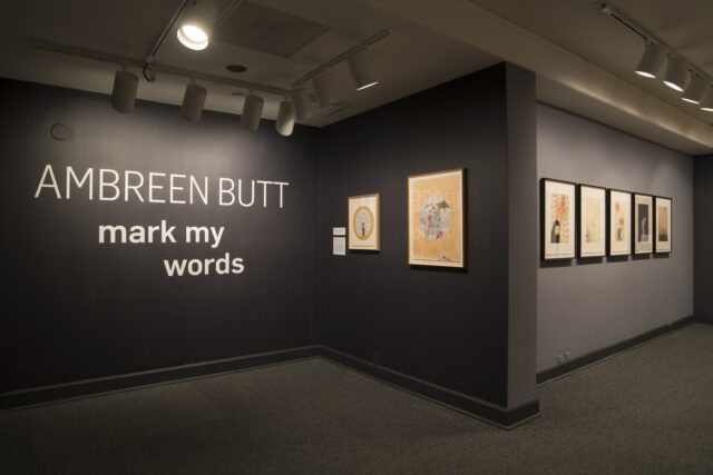 Museum gallery that shows seven prints against dark gray walls and intro text that reads 