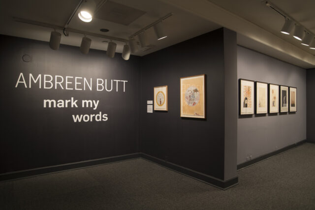 Museum gallery that shows seven prints against dark gray walls and intro text that reads "Ambreen Butt: Mark My Words."