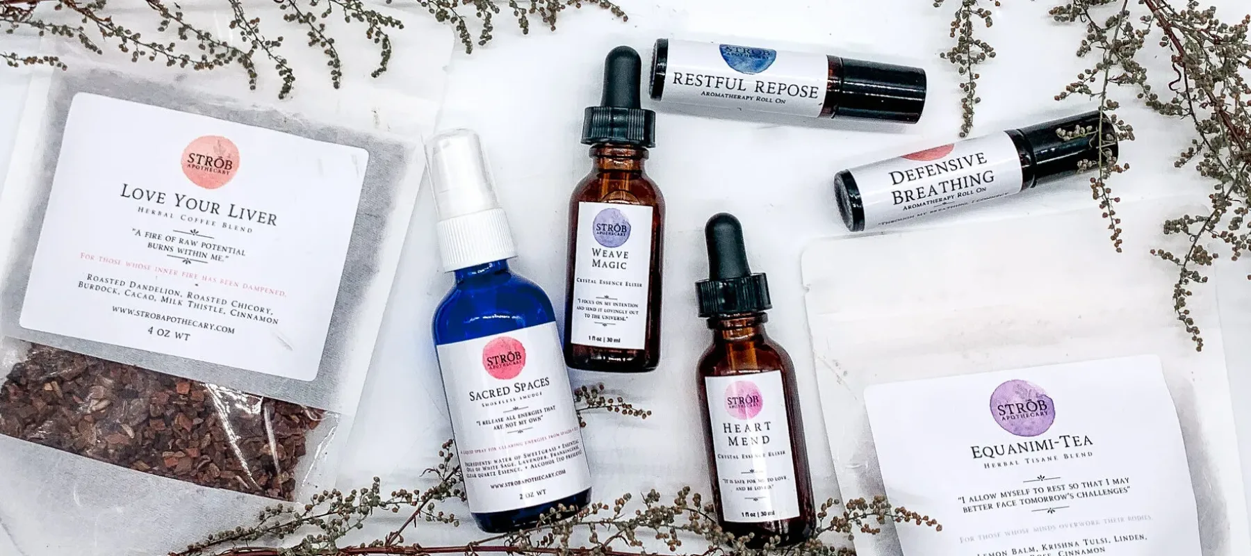 STRŌB Apothecary wellness products lying on a white background. The products are spray bottles, roll-on containers, bags of tea, and bottles with eyedroppers. Framing the products are delicate plant branches.