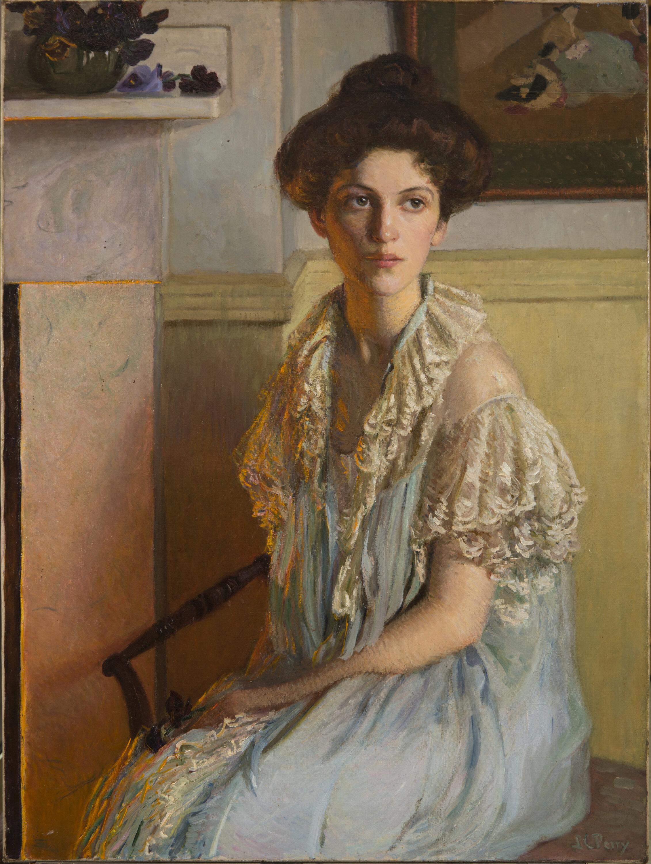 A young woman sits on a chair with her hair in a loose bun, wearing a white lace-trim gown. Her body turns slightly right towards a fireplace, its orange glow reflected on her hair and torso. The room is light and clean and a dark bowl overflowing with violets sits on the mantle.
