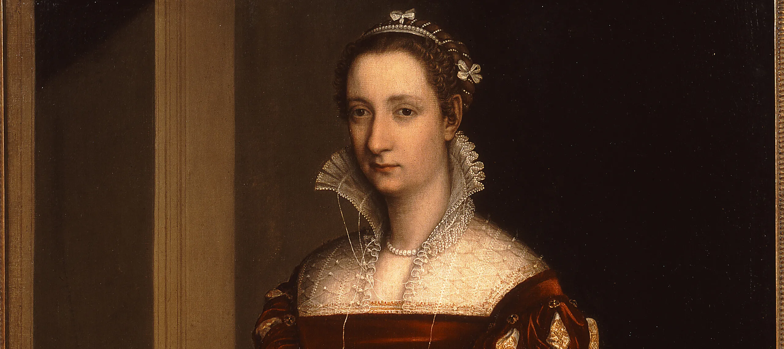 Three quarter length painting of a woman standing against a dark background. She is wearing a sumptuous red Renaissance-style dress with a high lace collar. Standing next to her at bottom left is a child holding a small spaniel.