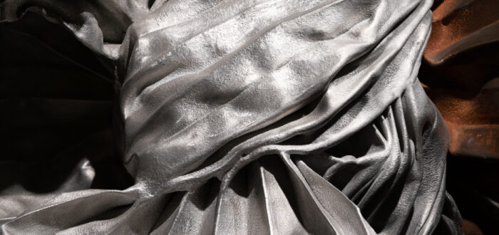 A close-up of a silver, metal sculpture that appears to be tied in a giant knot with crisp folds in the metal sheets.