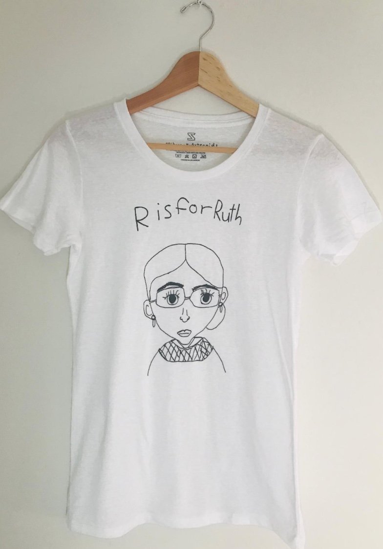 A white t-shirt with a simple pencil drawing of Ruth Bader Ginsburg's likeness. Above it, written in children's handwriting is the phrase "R is for Ruth."