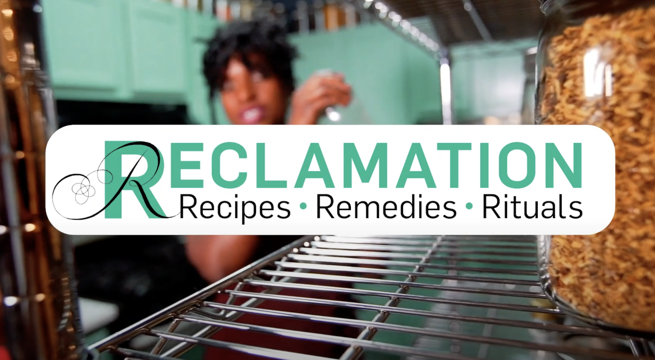 A white rectangle with green and black text that reads 'RECLAMATION: Recipes, Remedies, Rituals'. Behind the rectangle is a blurry image of a dark-skinned adult woman and her dark-skinned child in a turquoise-colored pantry, with a metal rack and a jar in the foreground to the right.