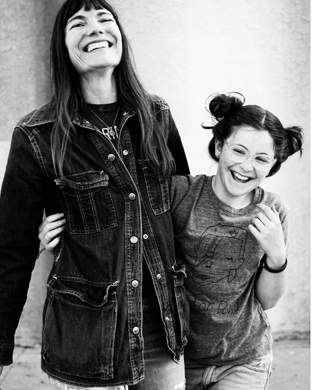 A black-and-white photo of a light-skinned mother and daughter, who have their arms around one another and are laughing joyfully.