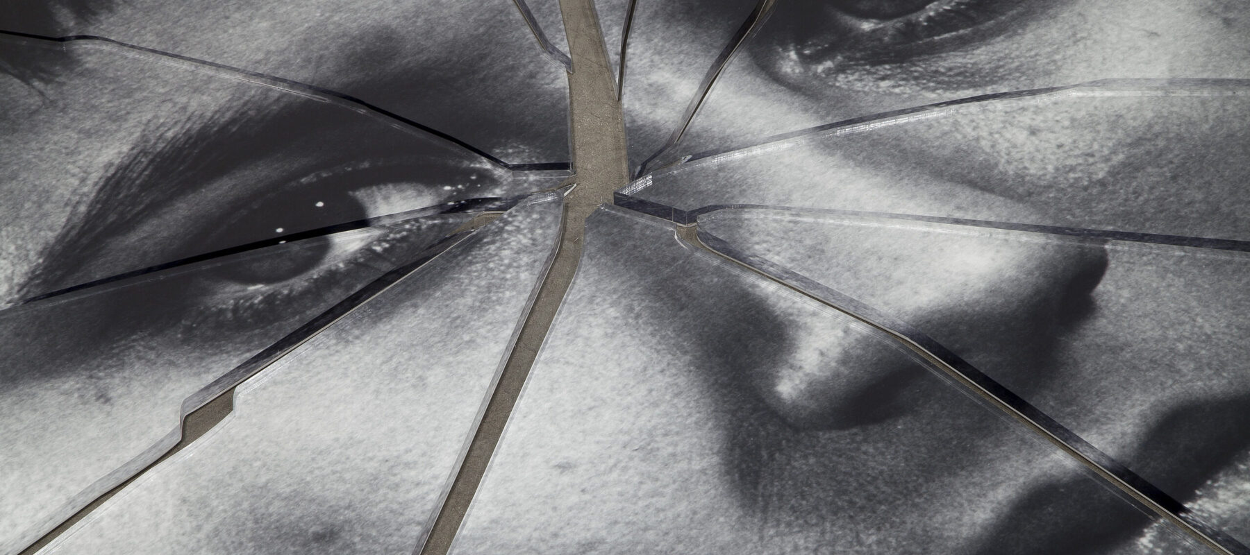A detail shot of a black-and-white image of a person’s face printed on plexiglas that has been shattered in the center.
