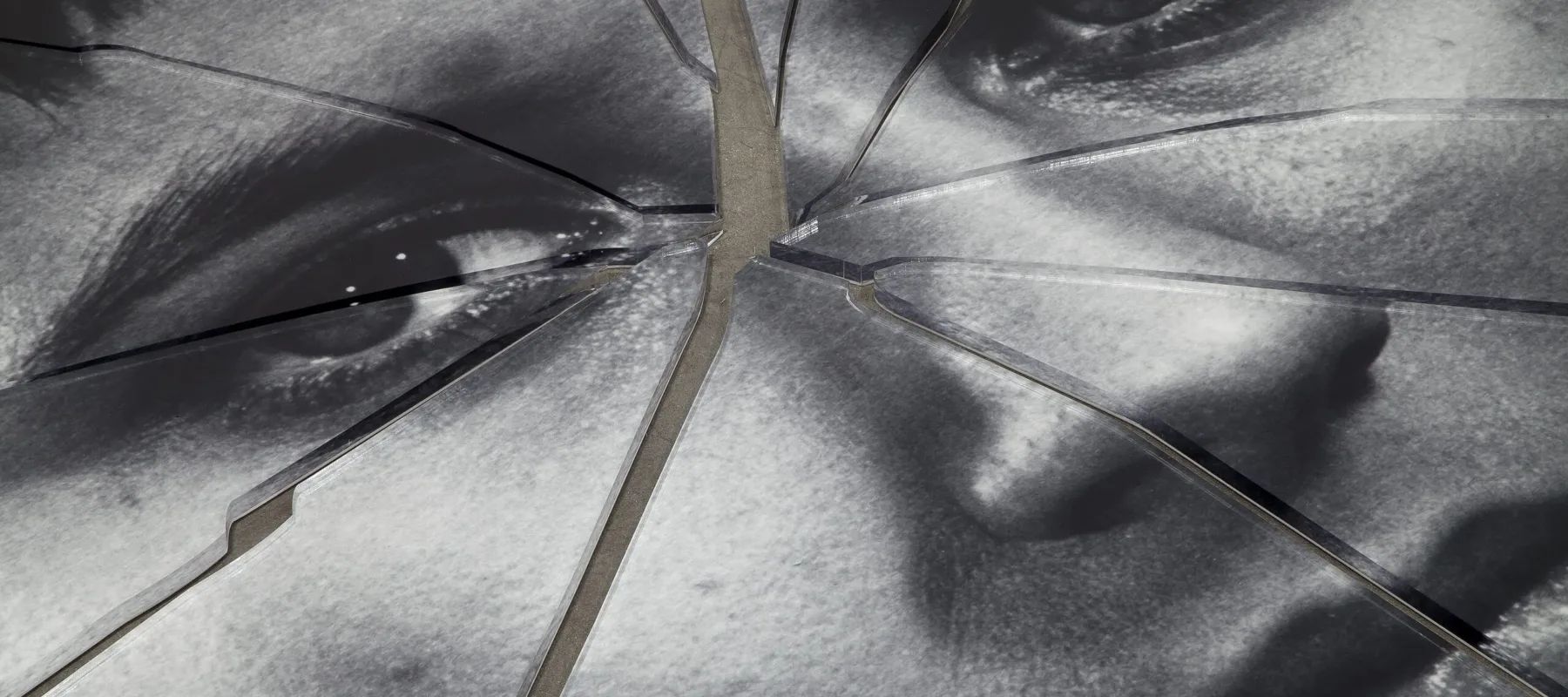 A detail shot of a black-and-white image of a person’s face printed on plexiglas that has been shattered in the center.