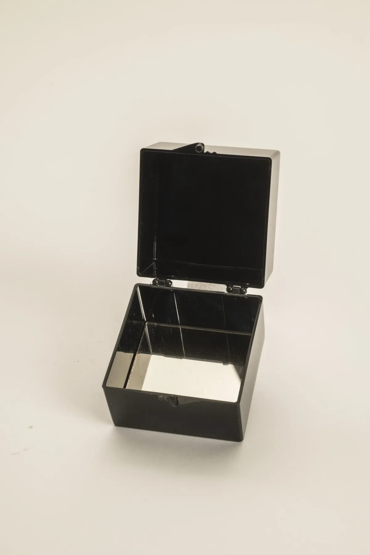 A small black plastic box that is opened to reveal a mirrored interior bottom.