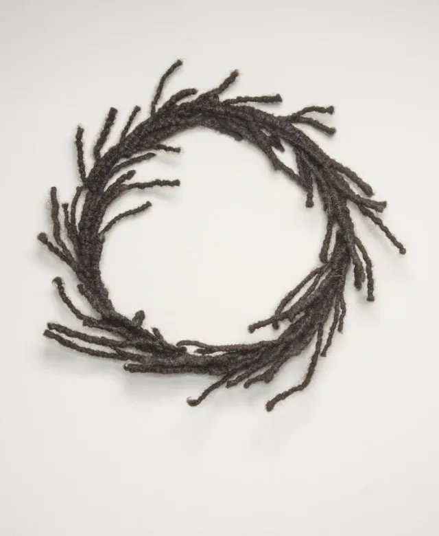 A circular wreath made of dark, tightly coiled hair with strands escaping and resembling laurels.