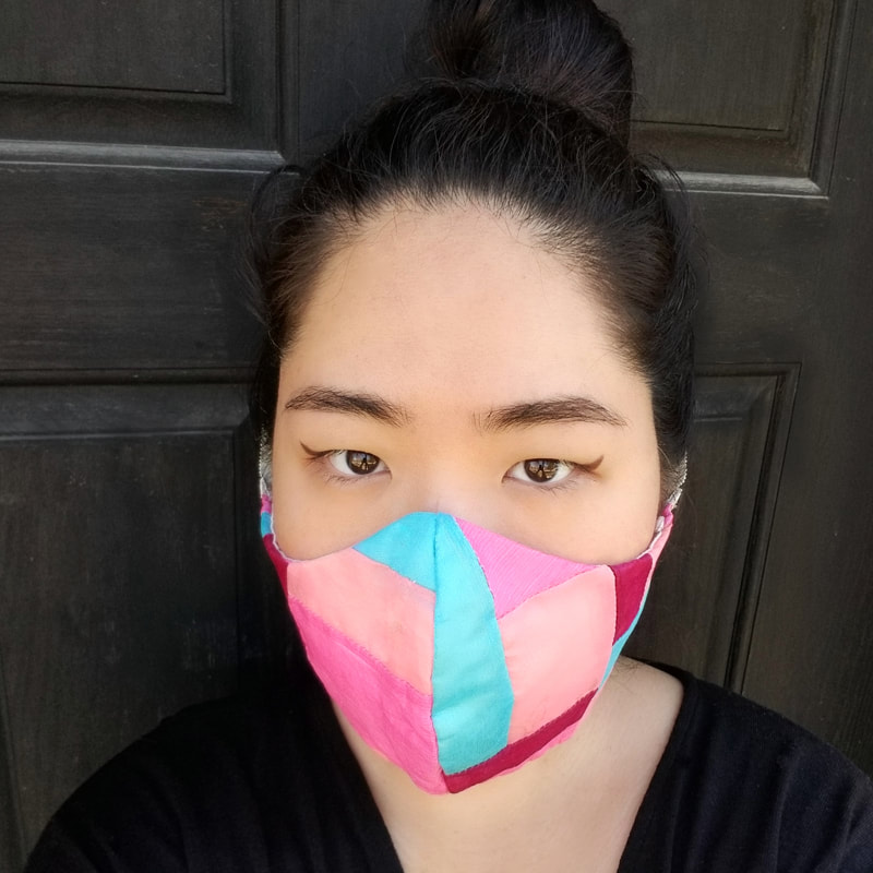 A light-skinned Asian woman wears a colorful patchwork face mask.