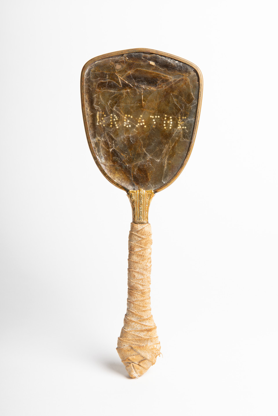 An antique hand mirror against a white background. The handle of the mirror is wrapped in light colored cloth. The head of the mirror is a brown, non-reflective material. The word “breathe” has been perforated onto the surface.