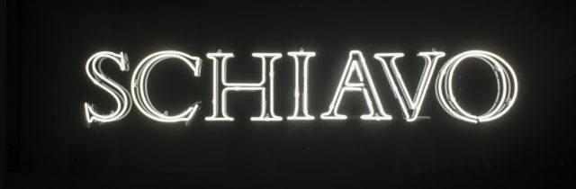 White neon letters against a black background. The letters light up to read “schiavo.”