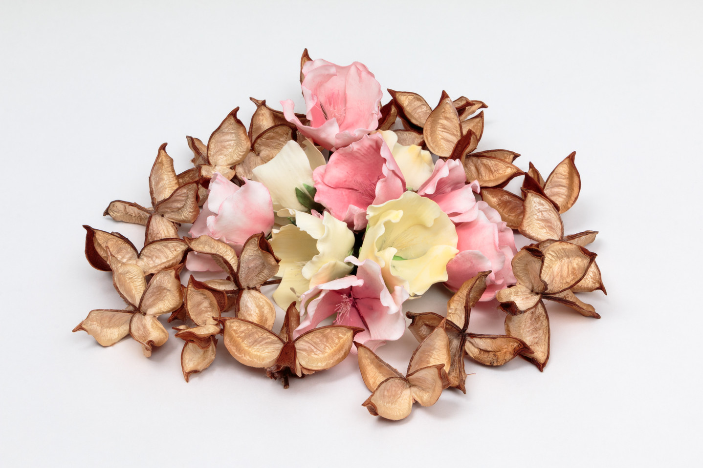 A ring of opened, delicate, pale brown cotton pods surrounding a small pile of creamy white and pastel pink flowers made of sugar.