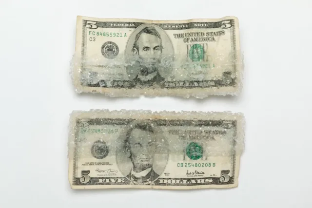 Two American five-dollar bills stacked on top of one another. Each one is half encased with crystalized sugar.