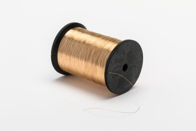 A sculpture of a spool of thread. The spool is made of black ebony, while the thin thread is gold. The thread Is wound tightly and neatly around the spool, and a small, thin tail sticks out the end.