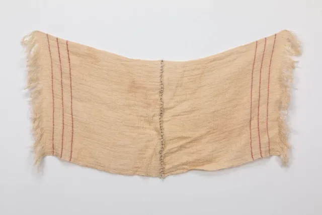 A rectangular, light colored sheet of fabric with three vertical red stripes on either end. The cloth drapes in the center, where two halves have been sewn together using black thread.