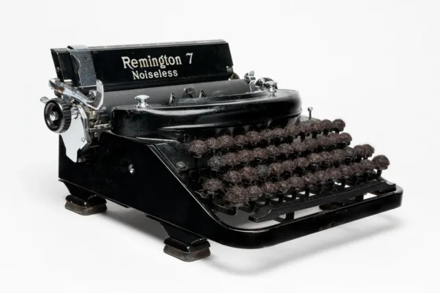 An antique, black and silver typewriter with the words 'Remington 7 Noiseless' emblazoned on the top. The lettered keys of the typewriter have been replaced with small balls of dark brown hair.