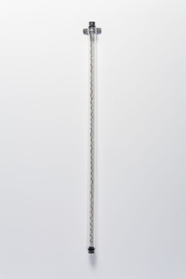 A sculpture of a glass tube affixed to a white wall with a spiraling column of small, multicolored glass beads. The beads are blue, red, yellow, green and black.