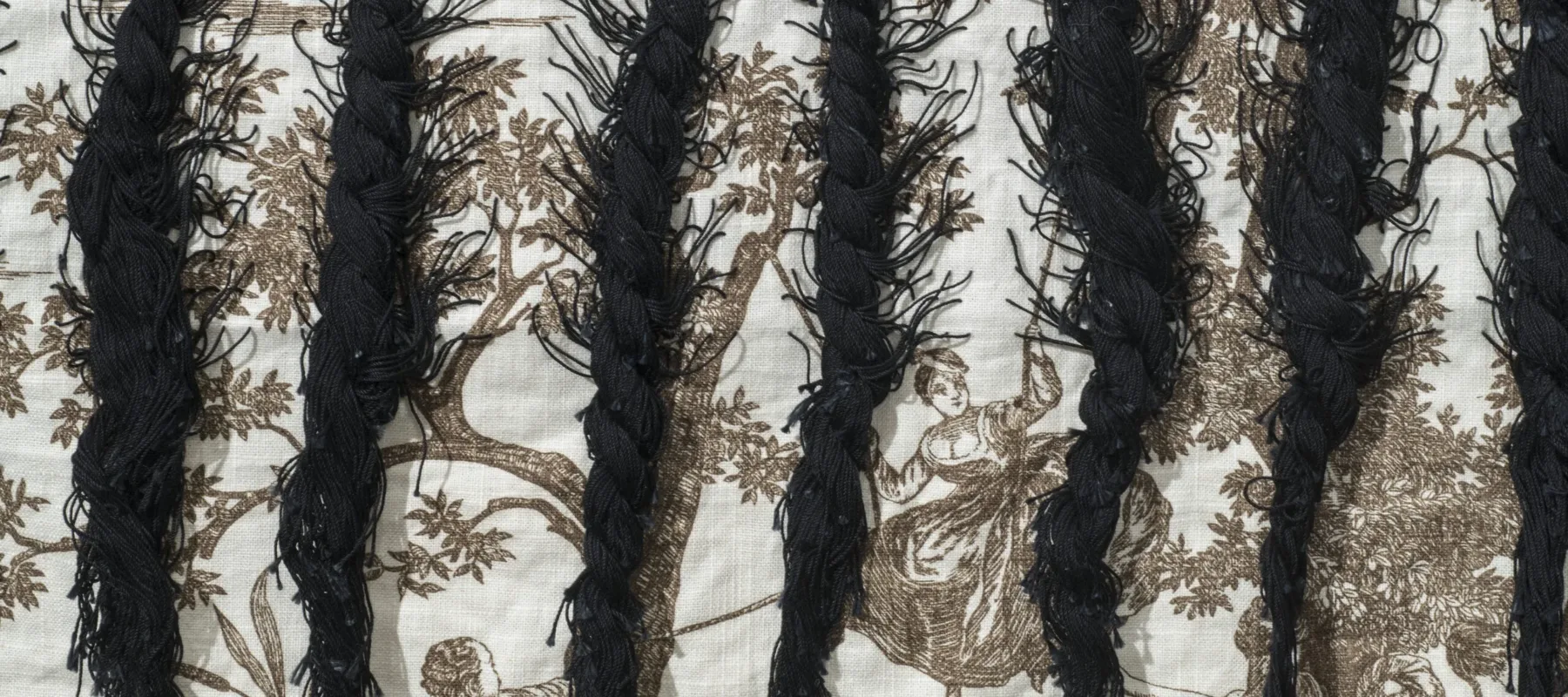 A close up photograph of braided black hair woven into cloth featuring colonial narrative scenes.