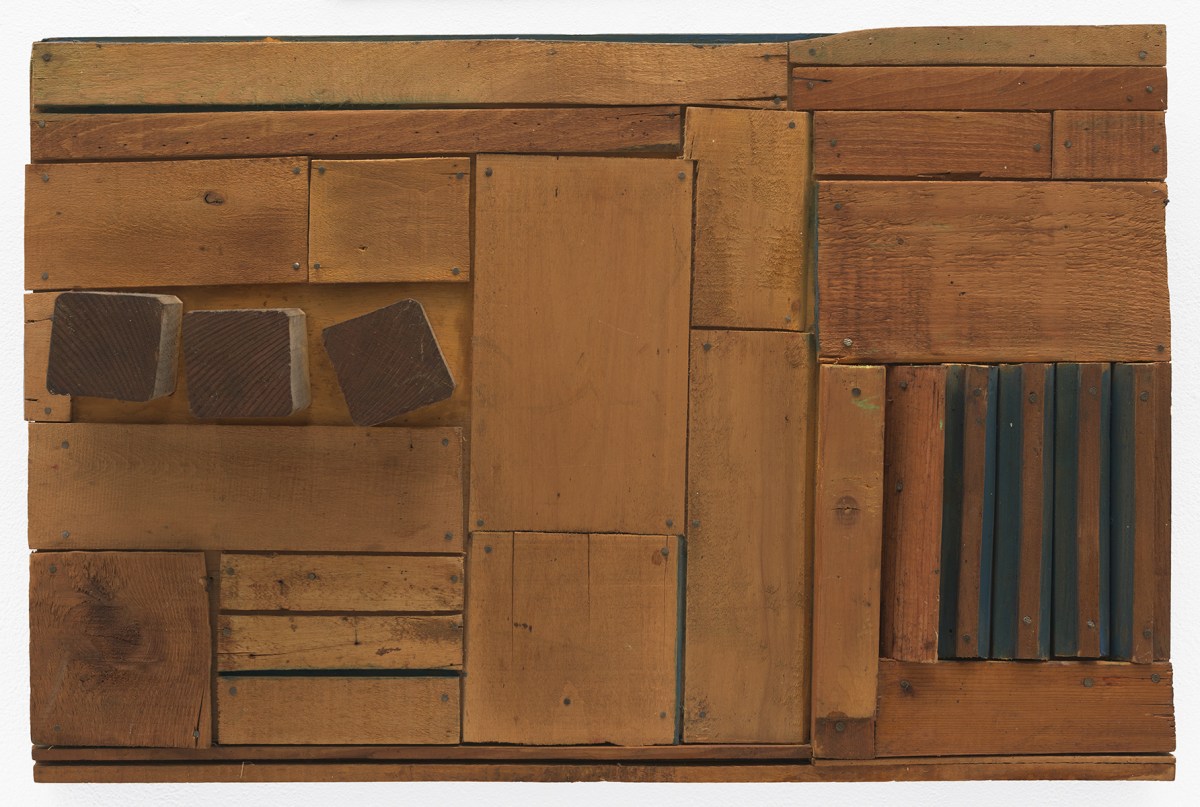 A wooden sculpture featuring brown, horizontal slabs cut in different lengths and widths atop which three square blocks are affixed in the left side, and the crevices of some of the slats are painted blue on the right side.