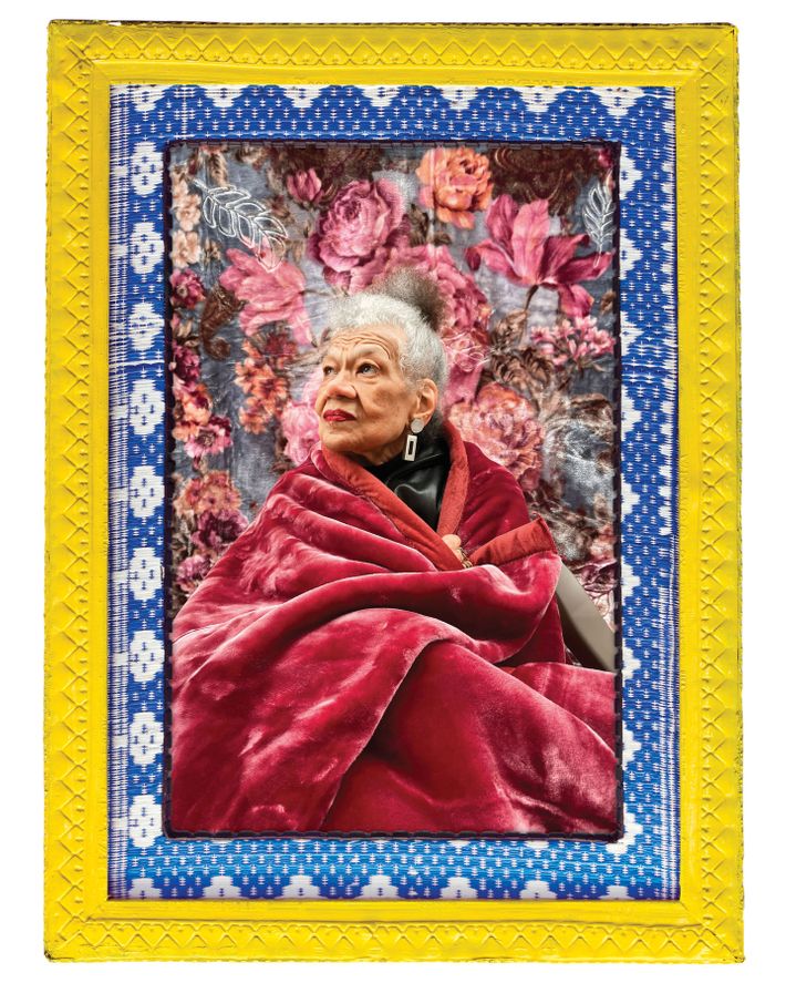 An older woman with gray/white hair worn up in a bun sits cloaked in a lush, deep pink, velvet blanket. She looks up to the left. Behind her is a floral wallpaper, which matches the blanket. The image is framed in yellow and blue geometric patterns.