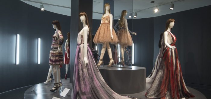 Four light skin mannequins display fashionable gowns of varying length on a circular platform.
