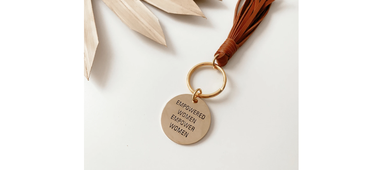 A small, circular brass keychain pendant is engraved with the phrase 