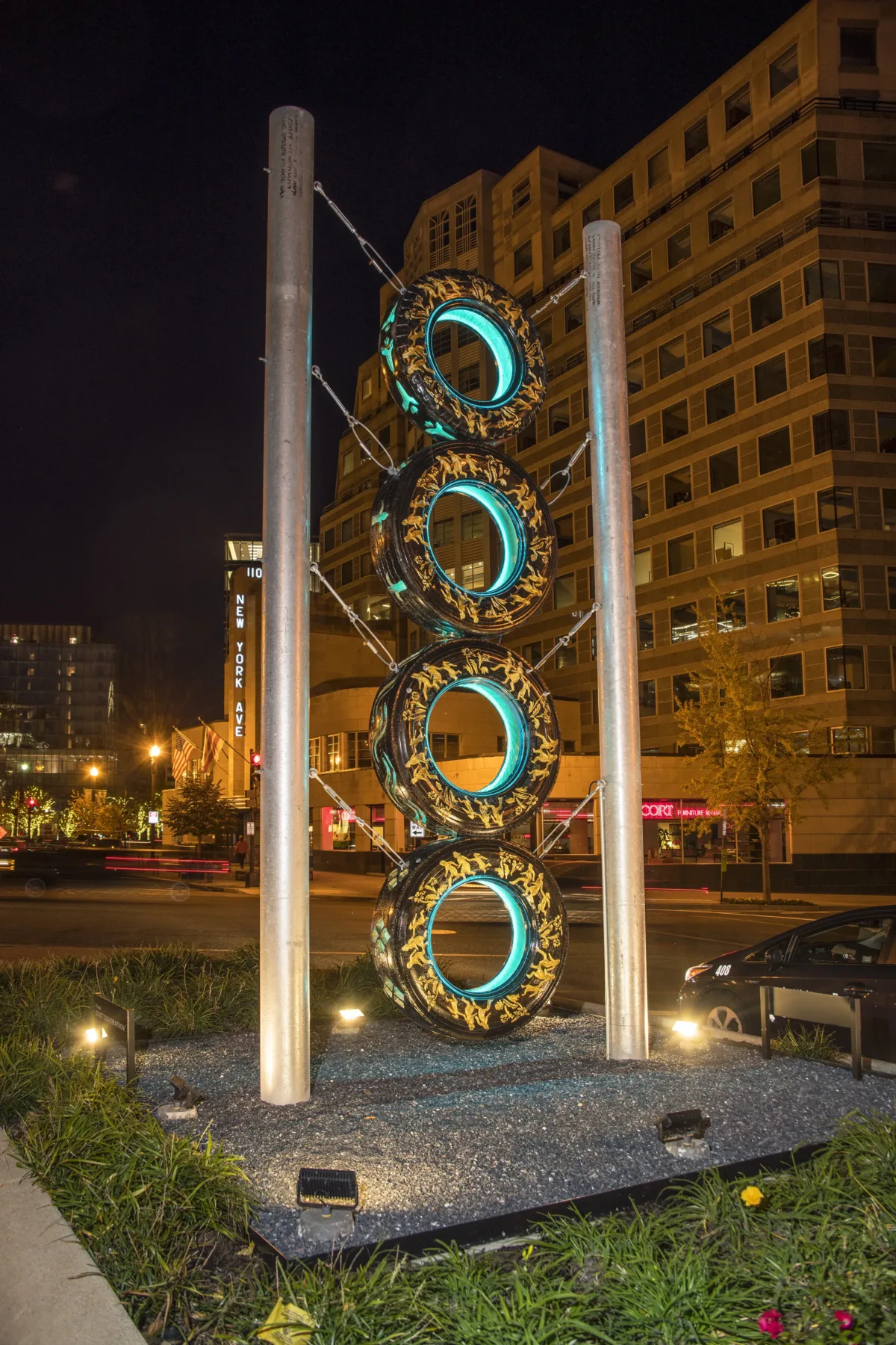 View of New York Avenue showing a tall, totem-like sculpture made of four stacked truck tires with gold leaf embellishments and supported by two steel poles.