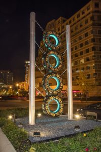 View of New York Avenue showing a tall, totem-like sculpture made of four stacked truck tires with gold leaf embellishments and supported by two steel poles.