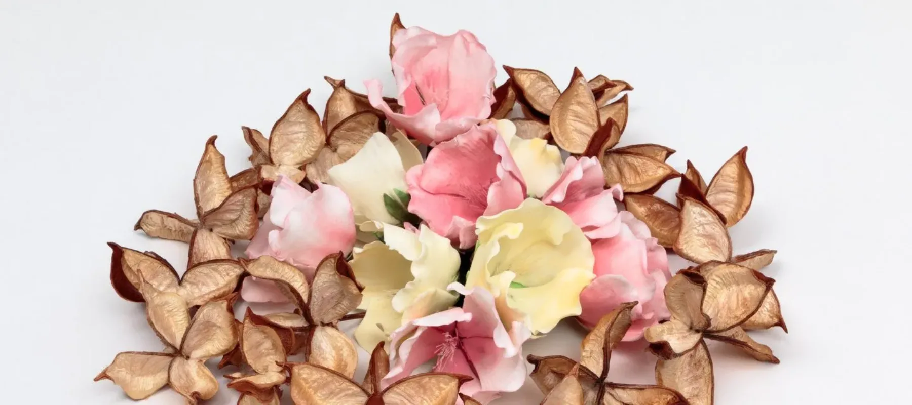 A ring of opened, delicate, pale brown cotton pods surrounding a small pile of creamy white and pastel pink flowers made of sugar.