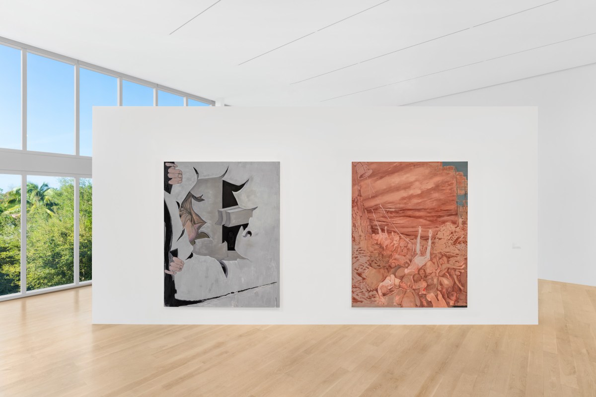 A large, airy gallery room with light wooden floors. A white, pop-up wall in the middle of the room features two abstract paintings. To the left is a wall of floor-to-ceiling windows that look out on green trees and a clear, blue sky.