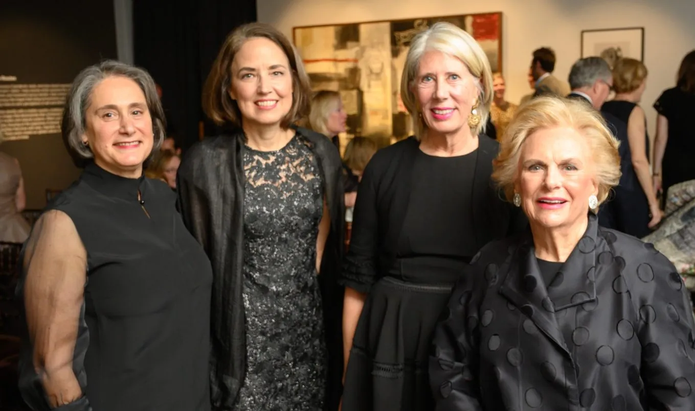 Four women with light skin wearing dark formal dresses pose for a photograph.