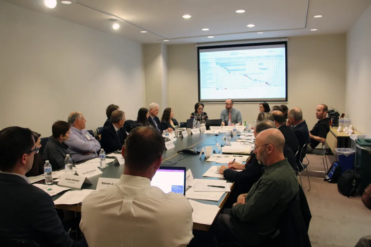 Multiple people attend a meeting around a large rectangular conference table.