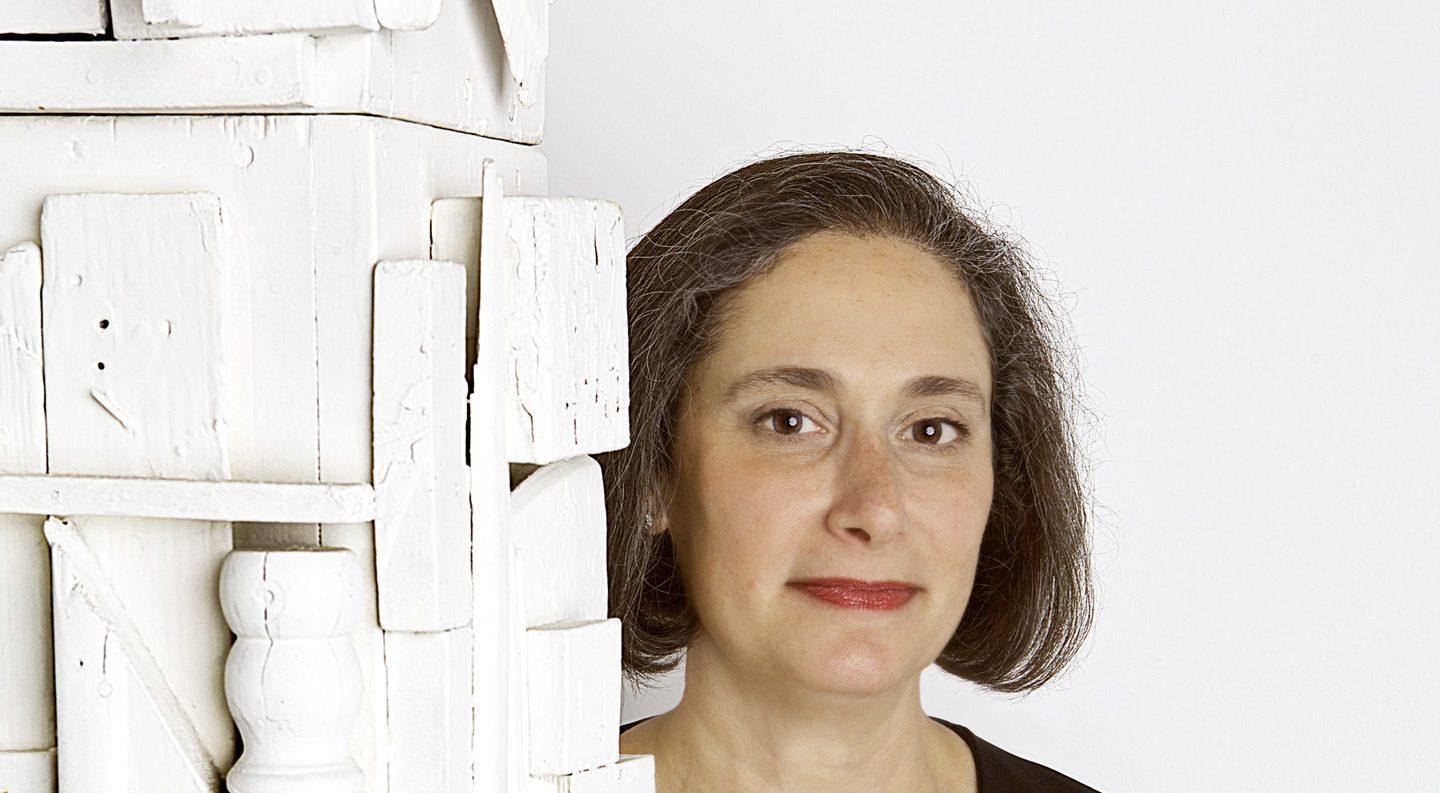 A woman with light skin and short brown hair posing behind a white assemblage sculpture.