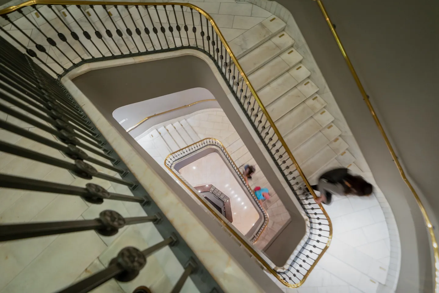 Photograph of the stairwell taken from the top looking down as two people are walking down the stairs.