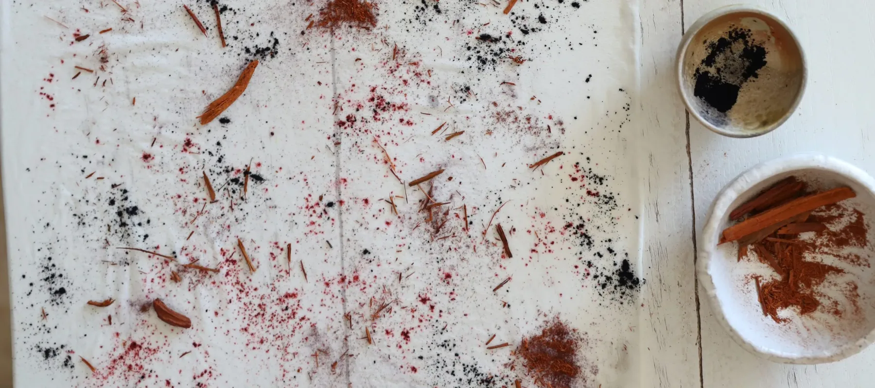 On a white wood table sit multiple mortars and a pestle with red ground herbs spread across the table.