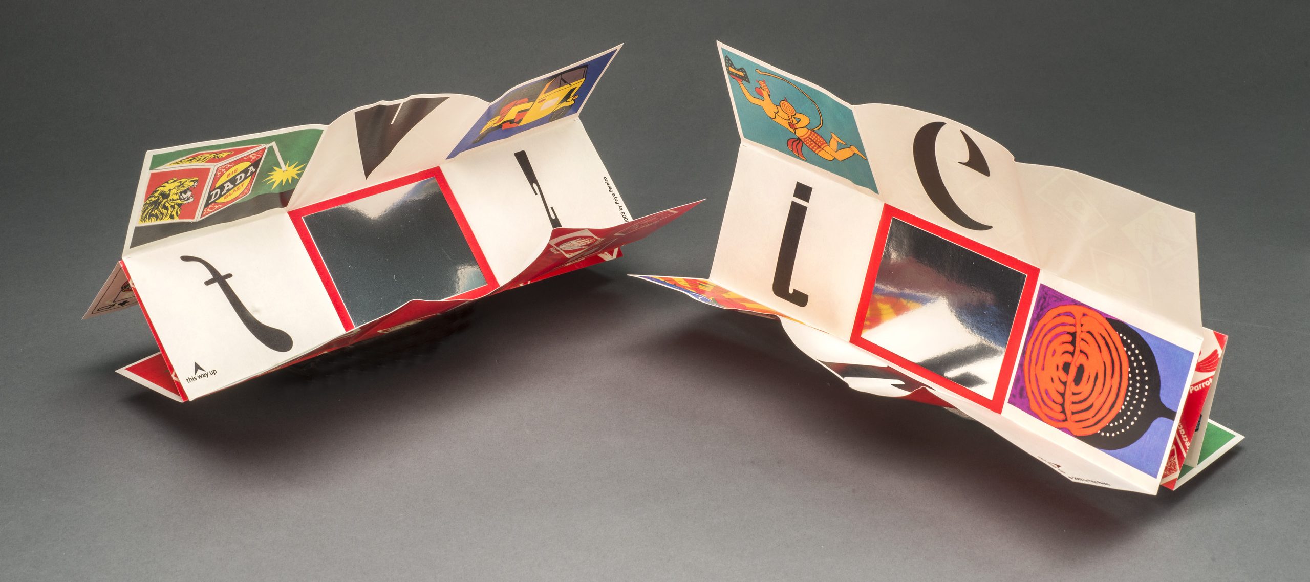 Two artists books with intricate folds and colorful panels sit side-by-side.